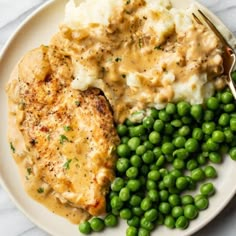 a white plate topped with chicken, mashed potatoes and green peas next to a fork