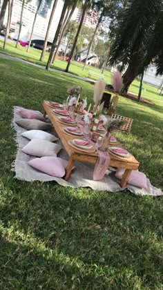 a picnic table set up in the grass with pink and white plates, napkins and place settings