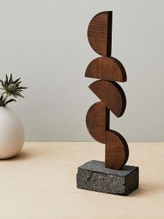 a wooden sculpture sitting on top of a table next to a white vase with a plant in it