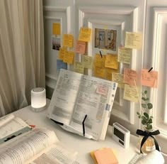 an open book sitting on top of a desk next to a window covered in sticky notes