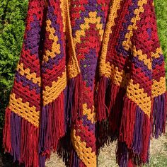 a colorful crocheted shawl hanging on a clothes line with grass in the background