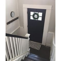 a black door with a wreath hanging on it's side next to a white stair case