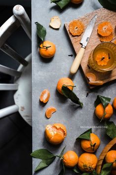 peeled oranges on a cutting board next to a knife and glass with liquid in it