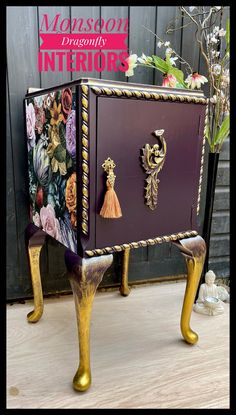 a purple and gold painted chest with tassels on it's legs, sitting in front of a wooden wall