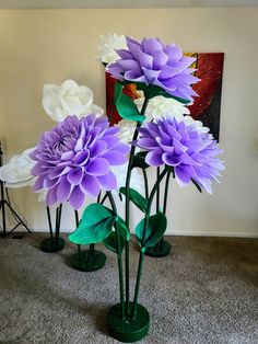 three purple and white flowers in green vases on carpeted floor next to wall