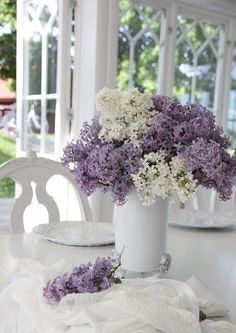 a white table with purple and white flowers in vases on top of the table