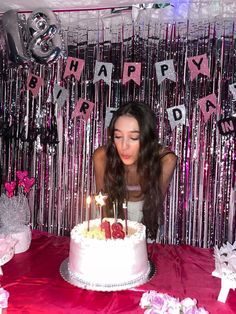 a woman blowing out candles on a birthday cake with pink and silver streamers behind her