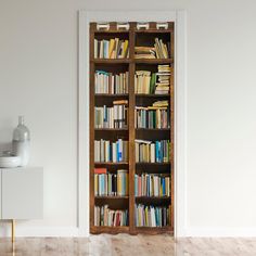 an open bookcase with many books on it in the corner of a white room