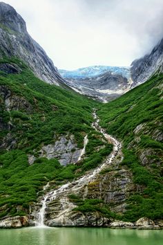 there is a waterfall in the middle of this green mountain range with water running down it