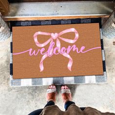 a person standing in front of a welcome mat with a pink ribbon on it that says welcome