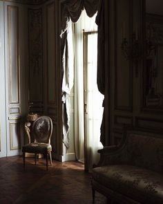 a chair sitting in the middle of a room next to a window with drapes on it