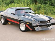 a black chevrolet camaro with red stripes parked in a parking lot next to trees