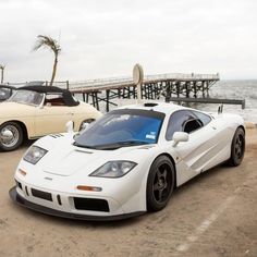 two sports cars parked next to each other near the ocean and pier on a cloudy day