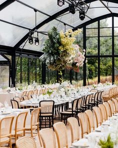 an indoor venue with tables, chairs and flowers hanging from the ceiling