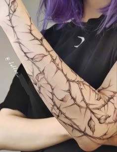 a woman with purple hair is holding her arm up to the camera and has branches on it