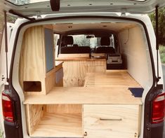 the back end of a white van with wooden shelves and drawers in it's cargo area