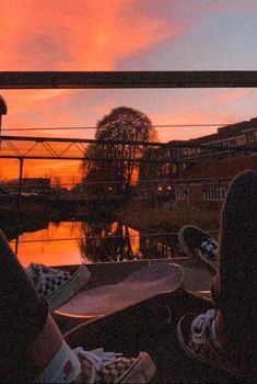 someone is sitting on their skateboard in front of the water at sunset or sunrise