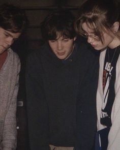 three young men are looking at something on a blue table with one man holding a pen