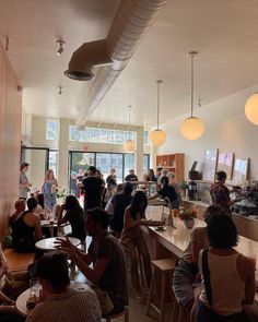 a group of people sitting at tables in a room with lights hanging from the ceiling