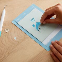 a person is cutting out some paper on top of a wooden table with a pen