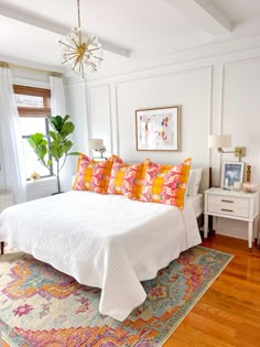 a white bed with colorful pillows and blankets on it in a bedroom next to a window