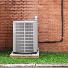 an air conditioner sitting in front of a brick wall next to a green lawn