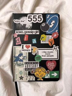 a notebook covered in stickers on top of a white bed sheet with the number 555