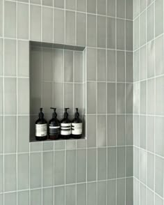 three soap dispensers are in the corner of a tiled shower stall, with white tiles on the walls