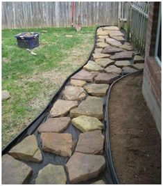 a stone path in the middle of a yard with grass and rocks on it, next to a fence