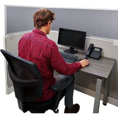 a man sitting at a desk with a phone and computer on it, in front of a cubicle wall