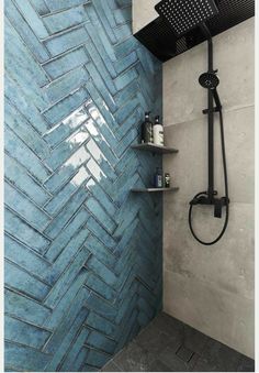 a shower with blue tiles on the wall and shelves in front of it, next to a shower head