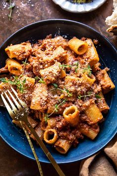 a blue plate topped with pasta and meat covered in sauce on top of a wooden table