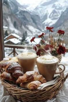 a wicker basket filled with pastries next to two cups of coffee on top of a table