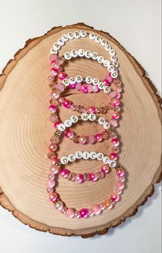 pink and white beaded bracelets with the letter e on them sitting on a wood slice