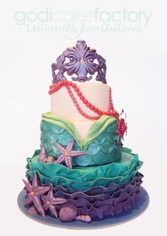 a three tiered cake is decorated with sea shells and mermaid tail decorations, along with pearls