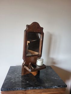 an old wooden mirror sitting on top of a black marble topped table next to a candle