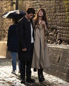 a man and woman standing next to each other under an umbrella on a cobblestone street