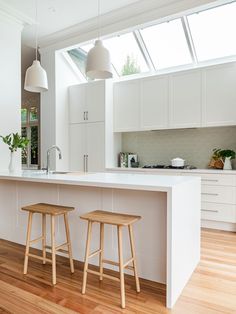 two stools sit in front of an island counter with white cabinetry and windows