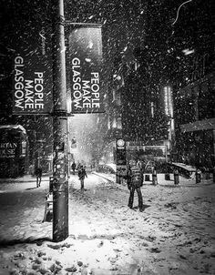 black and white photograph of people walking in the snow on a city street at night