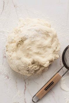 a ball of dough next to a whisk on a white counter top with a measuring spoon