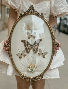 a woman holding up a framed artwork with butterflies on it's back and wings