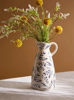 a blue and white vase with yellow flowers in it on a table cloth next to a brown wall