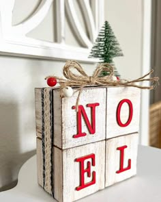 a wooden block with the word noel on it and a small christmas tree in the corner