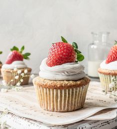 three cupcakes with white frosting and strawberries on top, sitting on a table