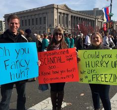 three people holding signs in the middle of a street with other people standing behind them