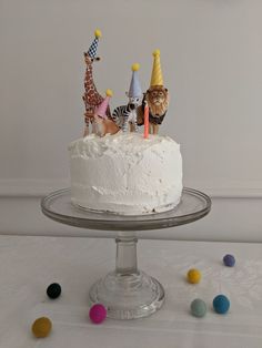 a white cake topped with frosting animals on top of a glass plate next to colorful candies