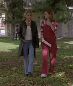 two women walking in the grass talking on their cell phones and one is wearing a red jumpsuit