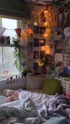 an unmade bed in front of a window with lots of pictures on the wall