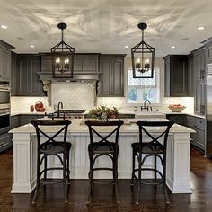 a large kitchen with gray cabinets and white counter tops, two bar stools at the center