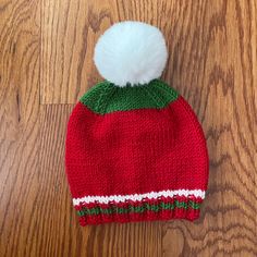 a red knitted hat with a green and white pom - pom on top